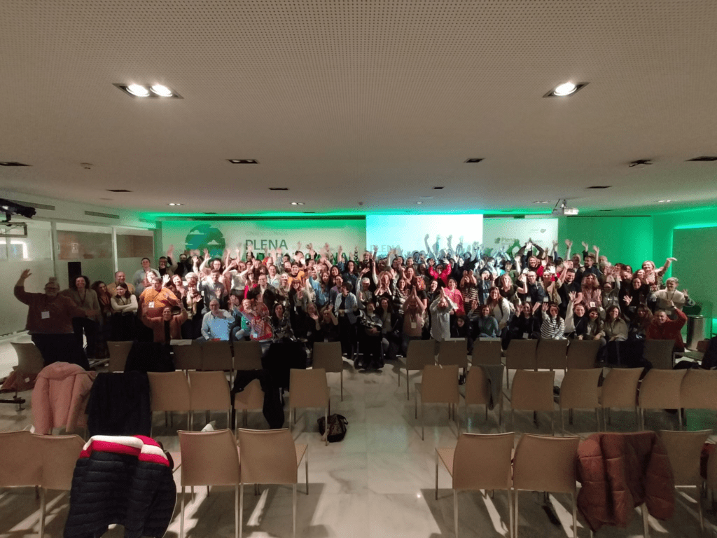 Foto final de participantes en el congreso de Plena Internacional. Un montón de gente levanta las manos